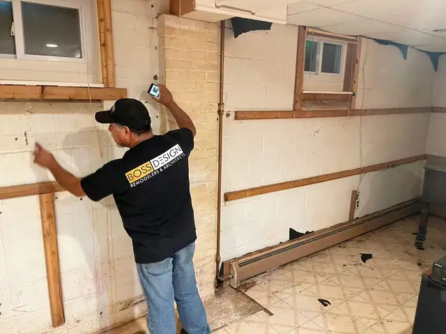 Boss Design crew member checking an opened basement wall at the start of a basement finishing project