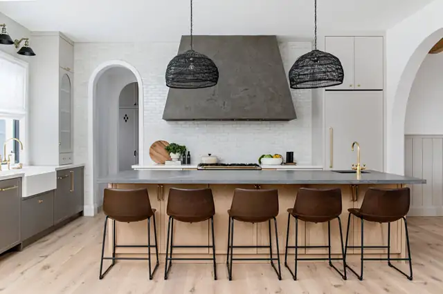 Kitchen with arched doorways, a gray plaster range hood, black woven pendants, farmhouse sink and leather counter stools