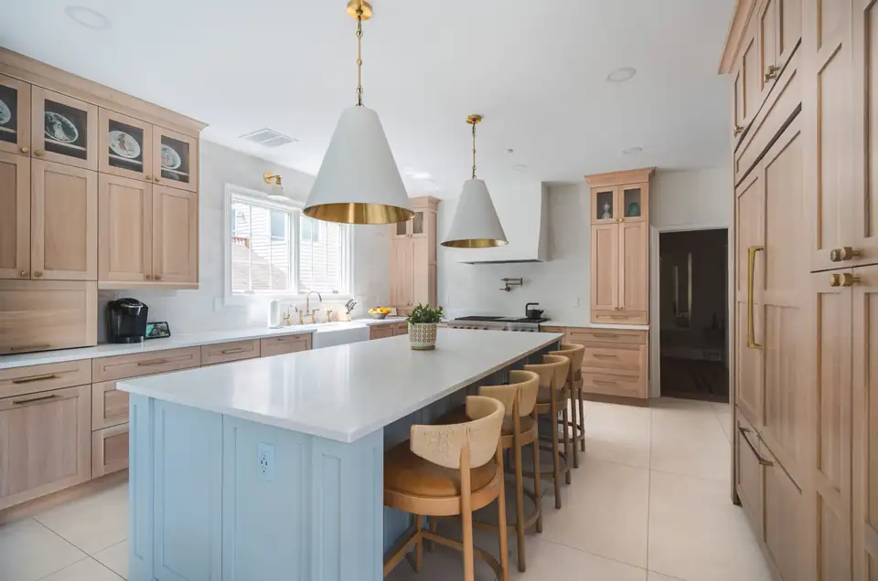 Kitchen remodeling Bethesda: Greentree Road kitchen with white oak cabinets, a pale blue island, white counters and white cone pendants with brass trim