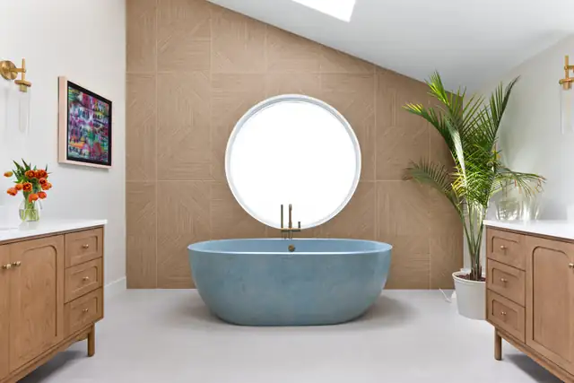 Potomac, MD primary bathroom with a blue stone freestanding tub under a round window, a patterned wood accent wall and oak vanities