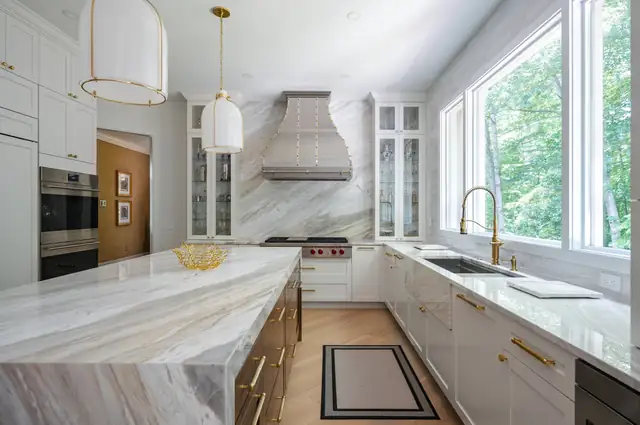 French-style kitchen with a quartzite waterfall island, white cabinets, brass hardware and a custom stainless range hood