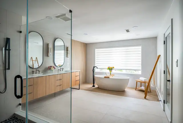 Primary bathroom by Boss Design Center with a floating wood double vanity, oval mirrors, a freestanding tub and a glass shower